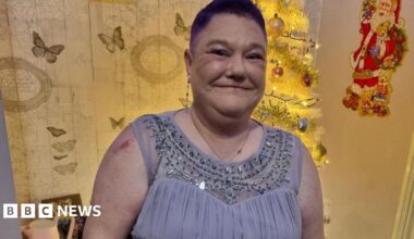 Annabell Downey has short cropped red hair and a long earing on her right lobe. She is wearing a light blue/grey dress with sequins around the neckline.