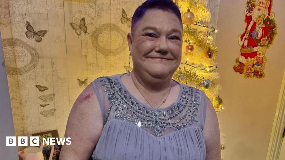 Annabell Downey has short cropped red hair and a long earing on her right lobe. She is wearing a light blue/grey dress with sequins around the neckline.