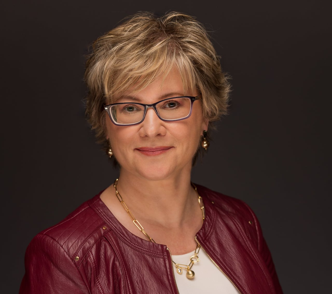 A woman with short hair and glasses poses for a picture.