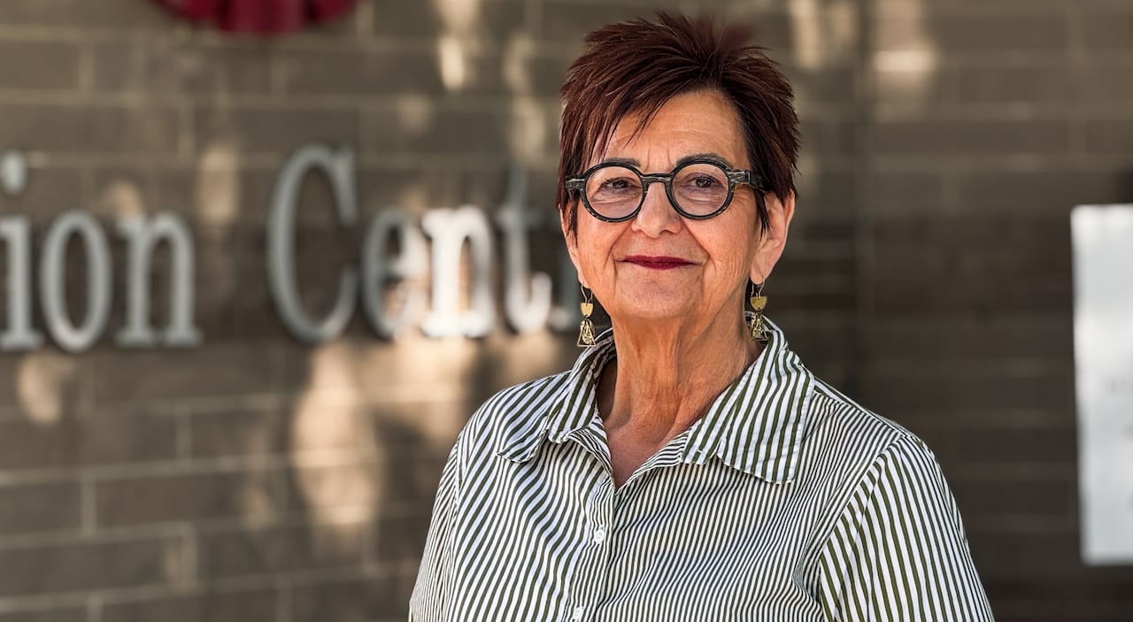 A woman in a striped shirt smiles at the camera. She is outside.