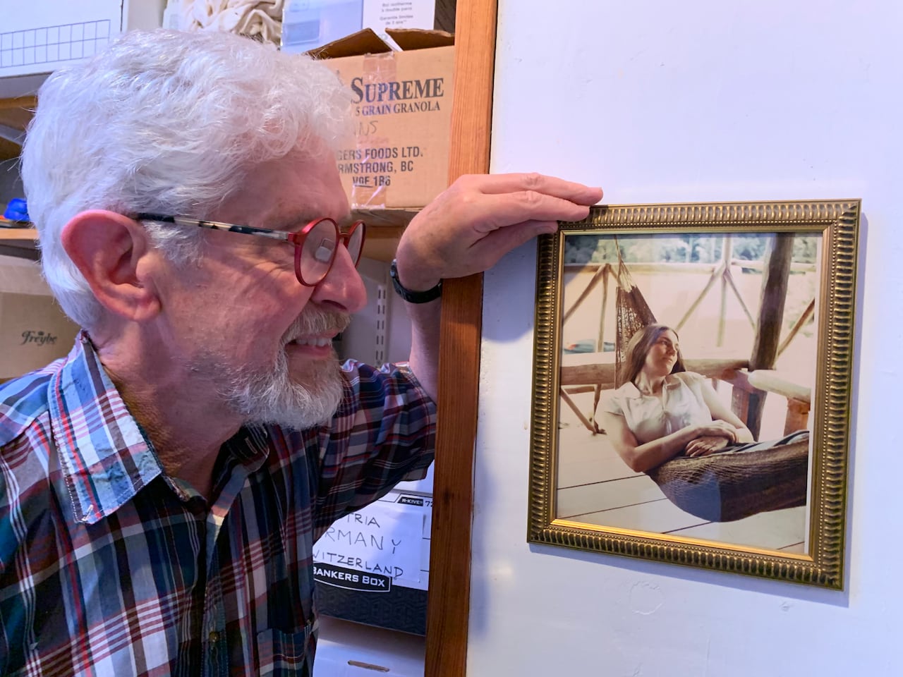 Grey-haired man looks at a framed photo of his wife on the wall