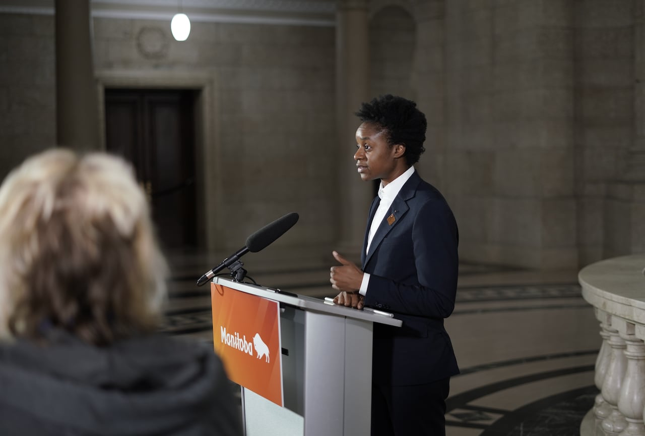 A person in a dark suit and white collared shirt speaks into a microphone mounted on a lectern.