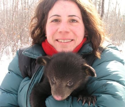 Woman in blue-green jacket holding a baby bear