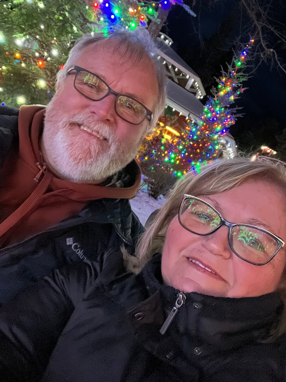 A white man with short white beard and white hair, wears glasses. He is standing next to a white woman with blonde hair, she is also wearing glasses.