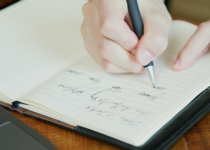 Close-up of a psychiatric institution worker's hand writing notes in a notebook during a memorable workday.