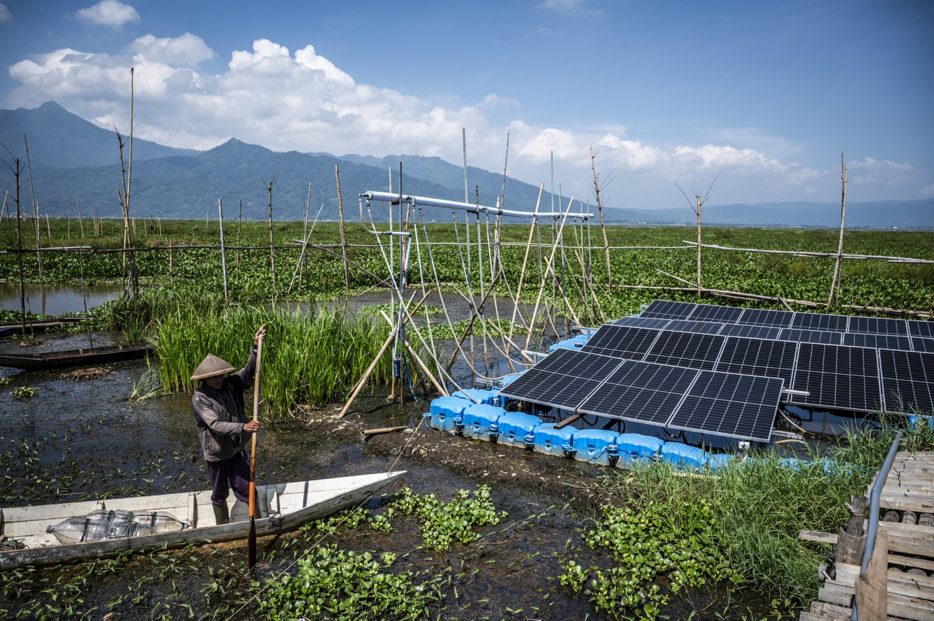 A farmer stands on a boat passing through solar panels on Oct. 12, installed as part of the Rawa Pening floating solar photovoltaic plant in Tuntang, Semarang regency, Central Java.