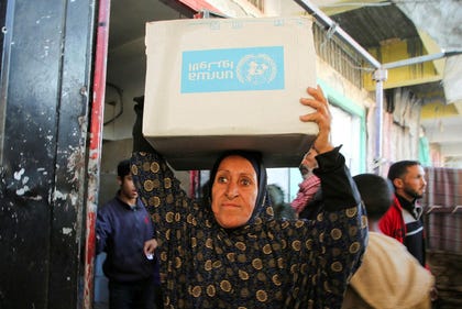 A Palestinian woman carries an aid box provided by UNRWA in Khan Yunis, in January 2025.