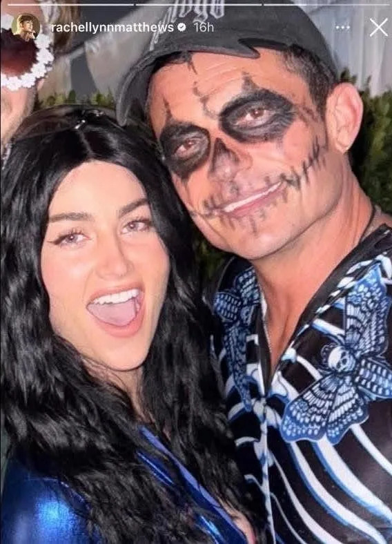 Two people smiling at a party. One wears a skeleton face paint and a shirt with a butterfly pattern; the other has long, wavy hair