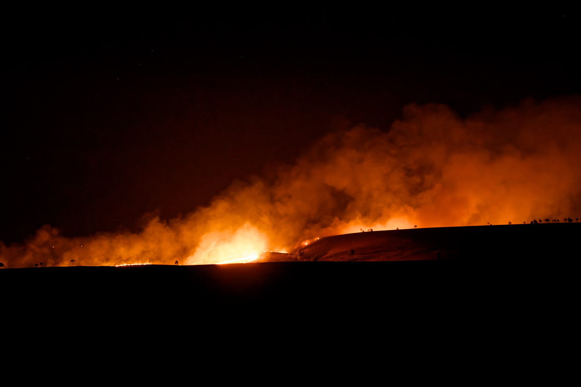 A bright orange fire and smoke seen on the horizon at night
