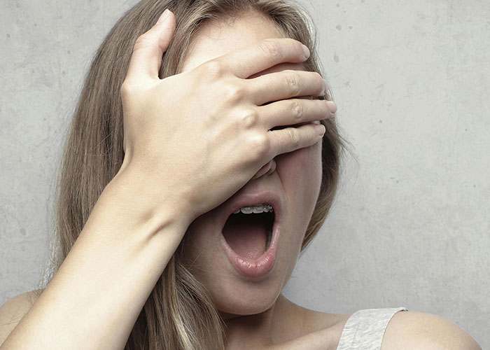 Woman covering her eyes with hand, mouth open in shock, illustrating unforgettable moments experienced by psychiatric institution workers.