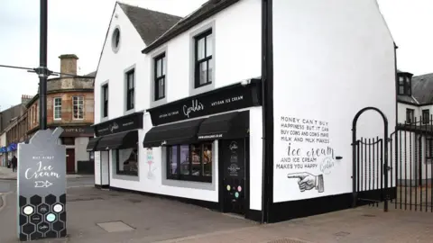 Geraldo's An ice cream and chocolate gift shop, with white and black walls and doors. A sign advertising ice cream sits outside it.