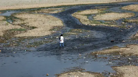EPA A woman stands by an almost entirely dried out river in Tehran that was once full 