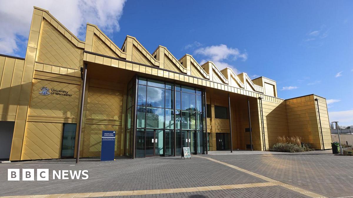 A multi-storey building with a shiny gold exterior and a large glass entrance is photographed on a sunny and largely clear day.