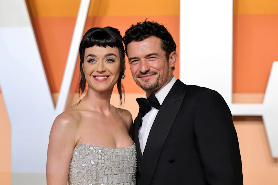 I don't know who these people are, but they're posing together on the red carpet; one is in a strapless dress, and the other is wearing a tuxedo