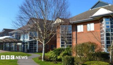 A hospital building. There are trees and shrubs in front of the building.
