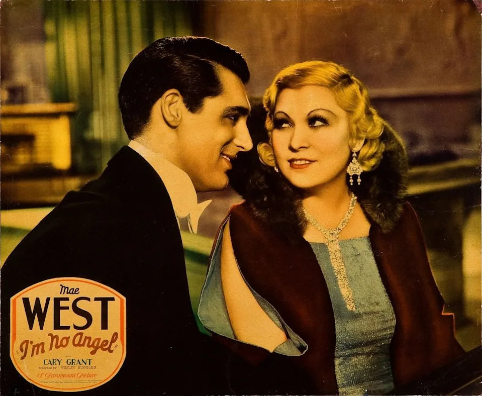 Mae West and Cary Grant in "I'm No Angel" promotional image; West wears a glamorous gown with a fur stole and jewelry, in a classic film setting