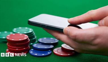 A hand holding a black smartphone, hovering over a selection of green, red and blue poker chips