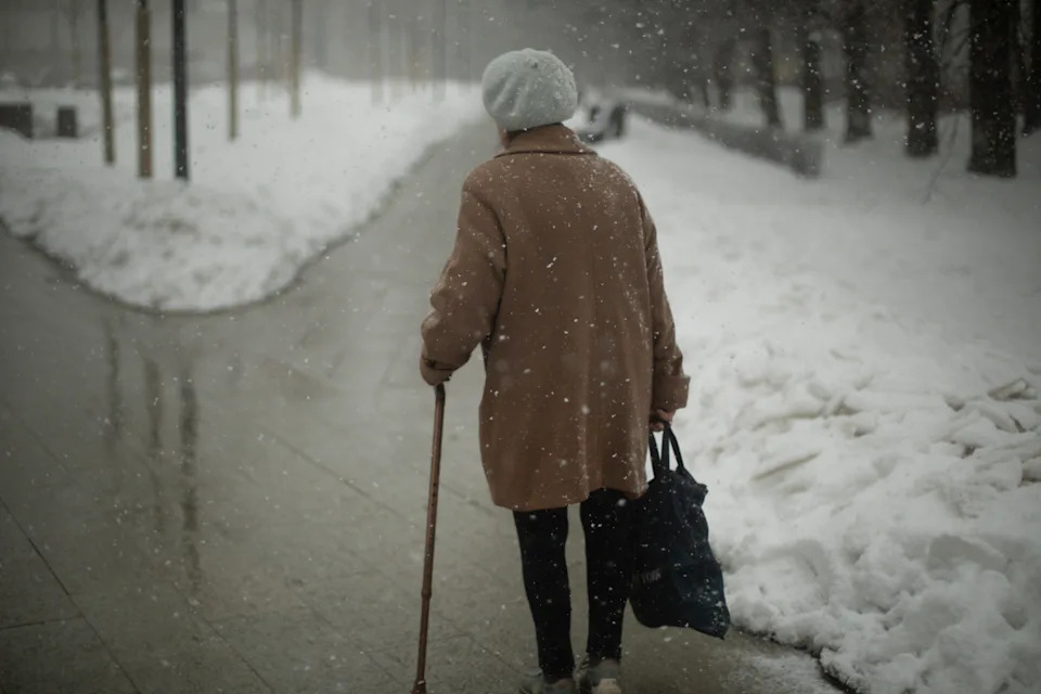 Woman with walking stick. Pensioner walks down road. Grandmother on street in Russia. Old age in city.