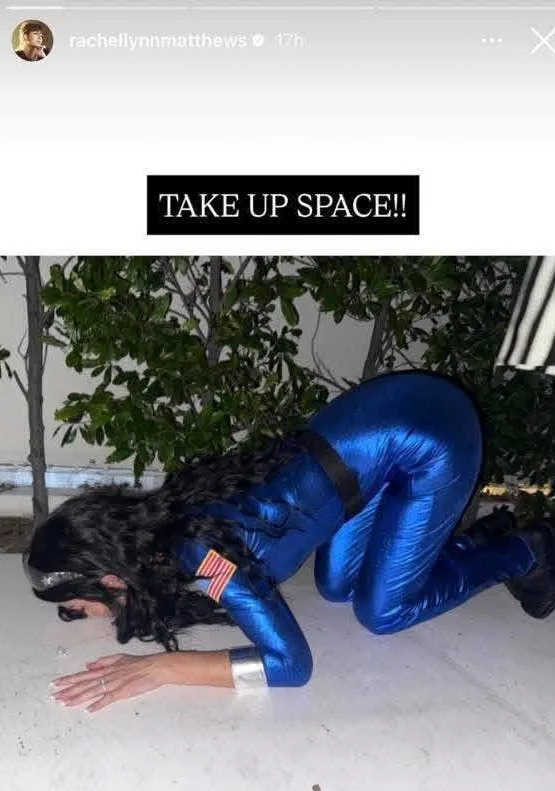 Person in a shiny space-themed outfit mimicking a crawling pose indoors, with the text "Take Up Space!!" above
