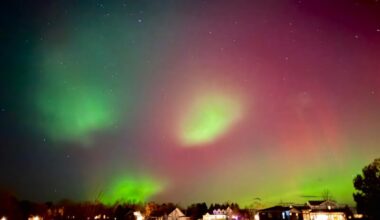 Aurora blobs: Vertical red and green streaks of aurora with bright green blobs in the foreground above a neighborhood.