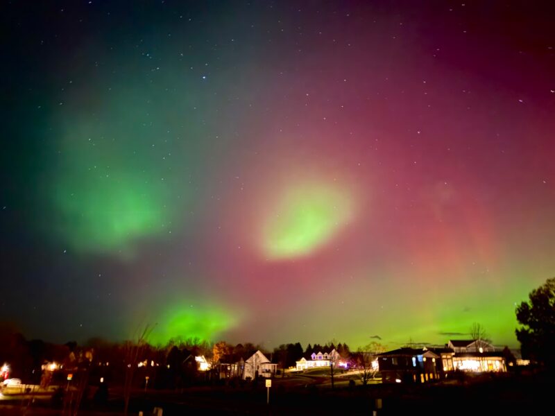 Aurora blobs: Vertical red and green streaks of aurora with bright green blobs in the foreground above a neighborhood.