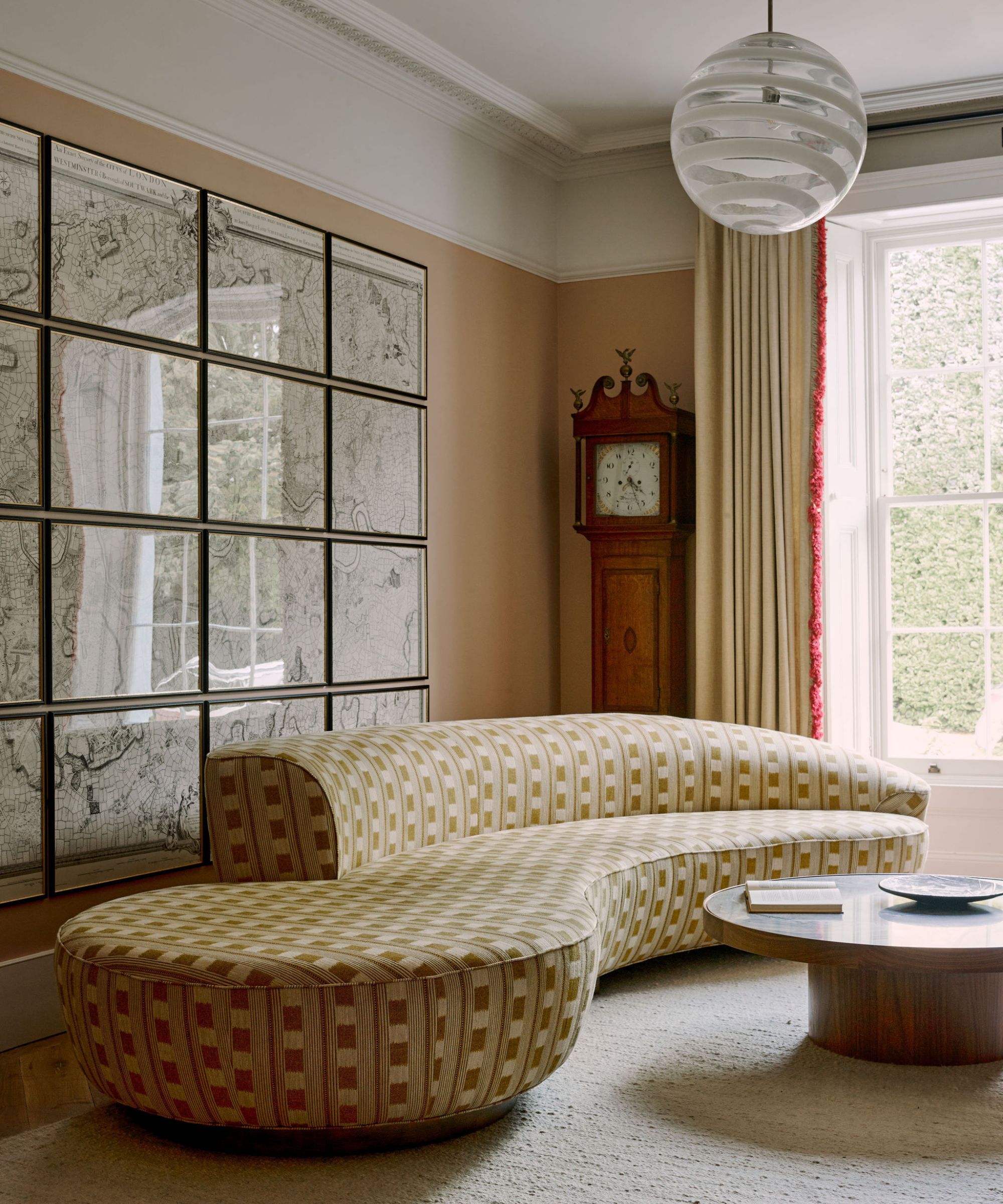 modern warm yellow living room with a large window, large curved yellow printed couch with an antique wooden clock and marble coffee table