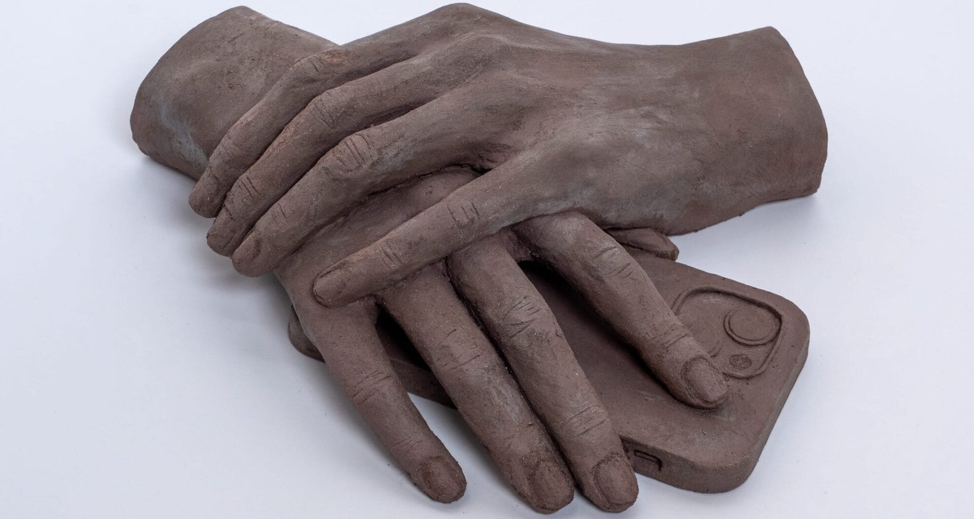 a clay sculpture by Léonore Chastagner of two hands folded over a smartphone