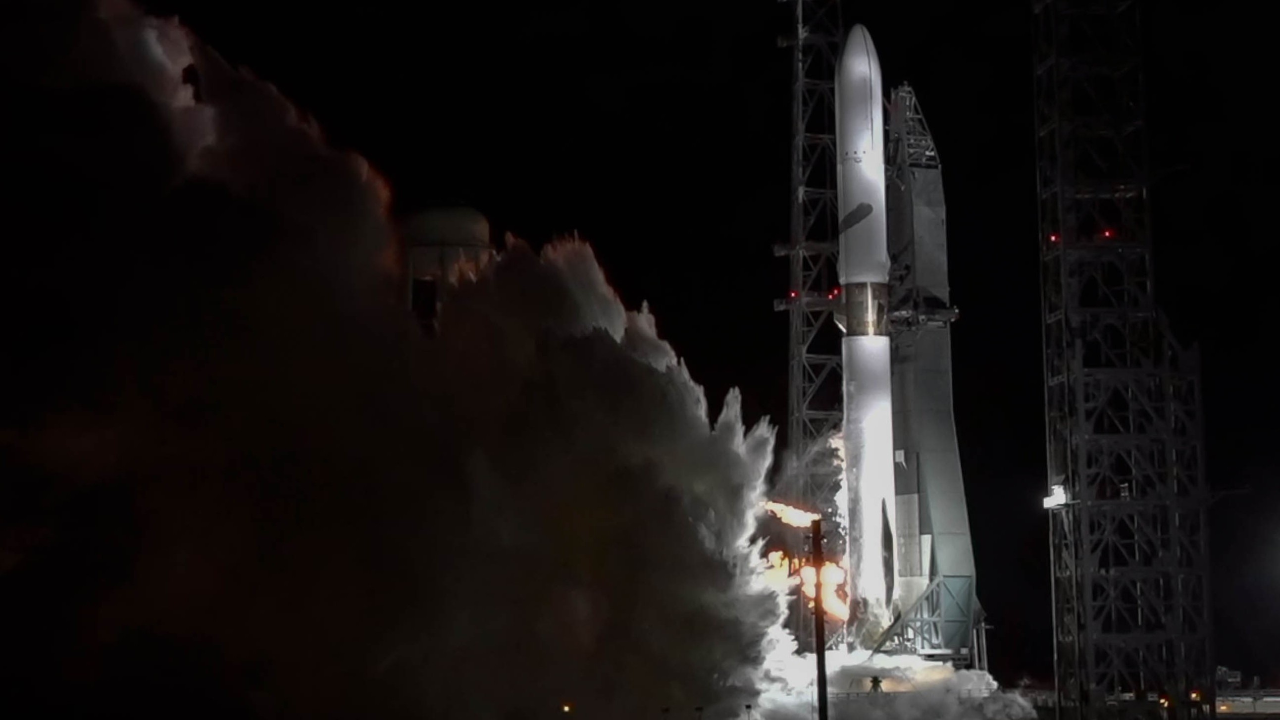 A tall white rocket spits smoke from below as its engines fire.