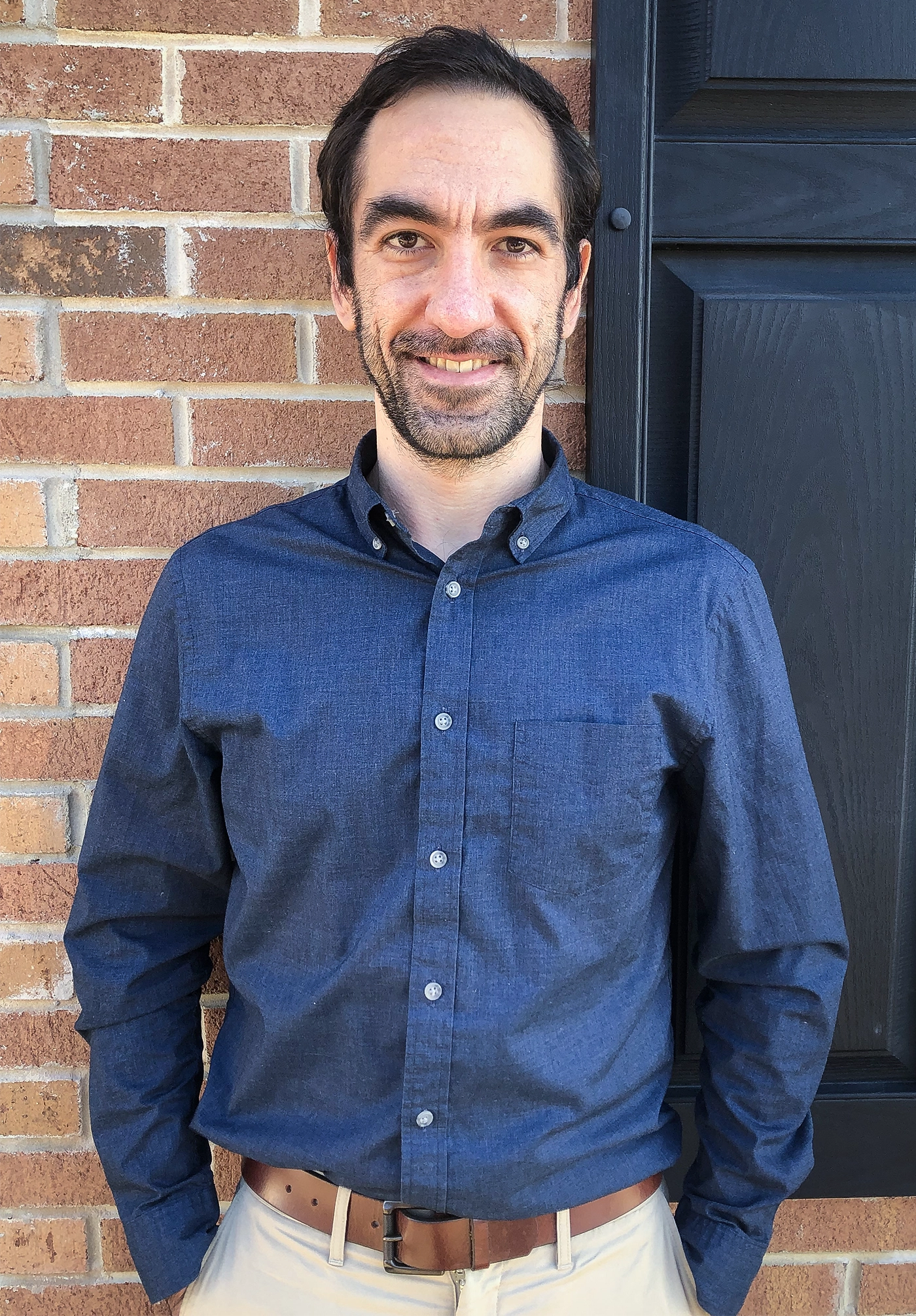 A man in a blue shirt before a brick wall.