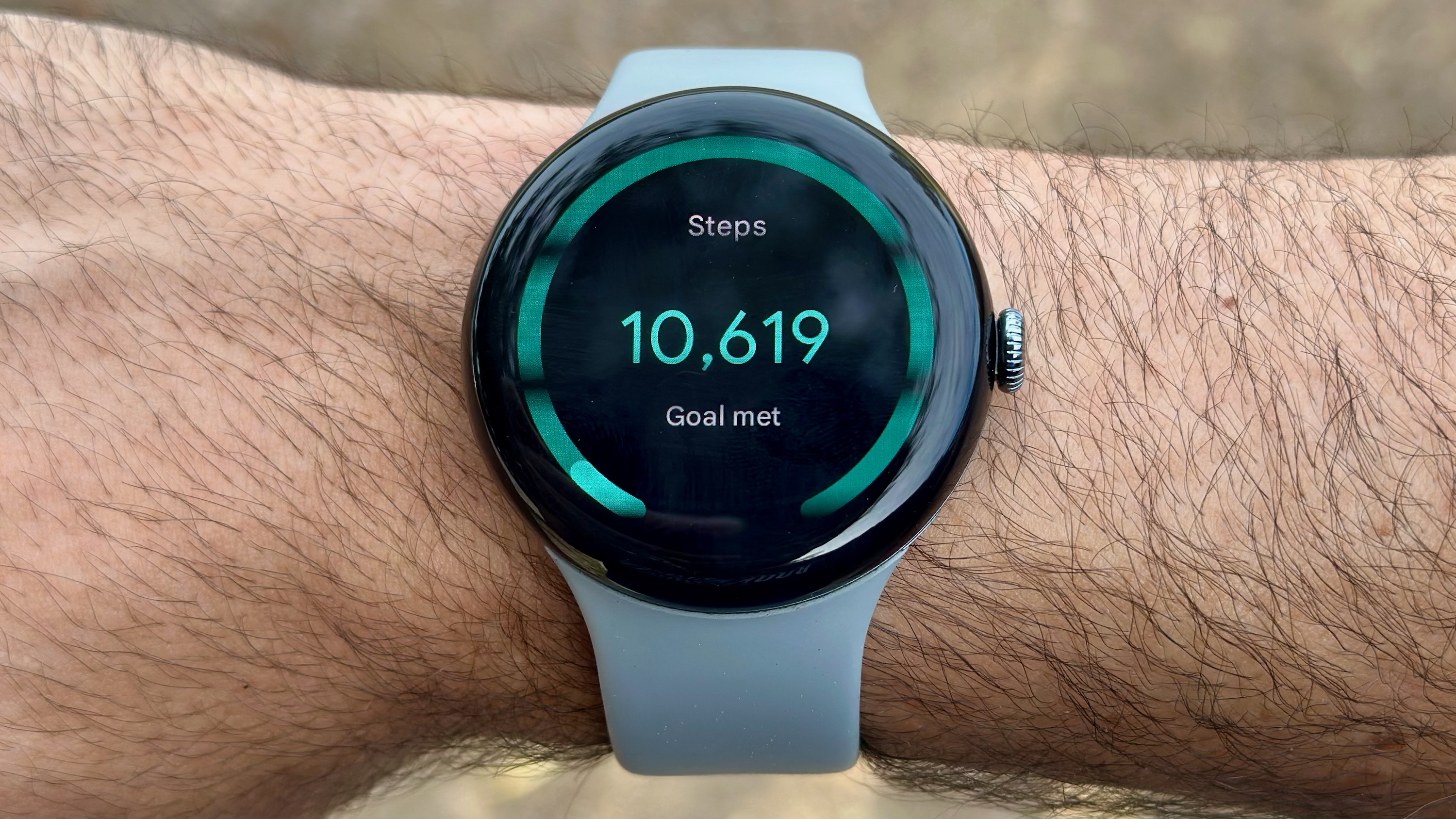 The Google Pixel Watch 3 on a wrist showing the Steps Tile, with 10,619 steps (Goal met)