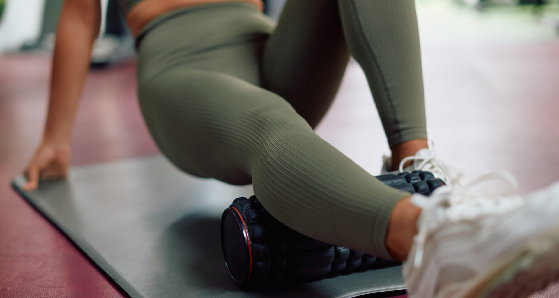 Close-up of athlete massaging her leg with foam roller in a gym.