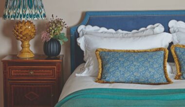 Cream bedroom with blue headboard and white bedding with a wooden bedside table and yellow lamp