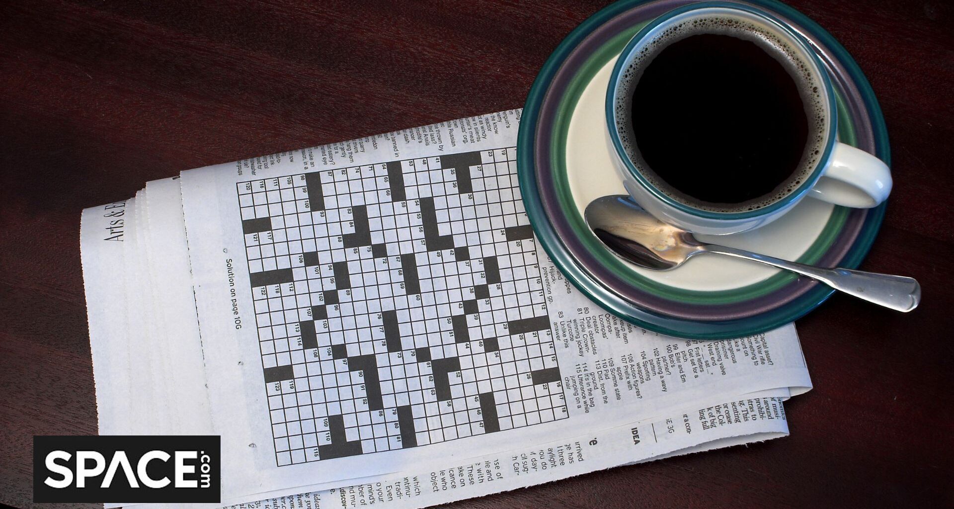 A black and white crossword puzzle sits underneath a blue and white coffee cup with the Space.com black and white logo in the bottom left corner.