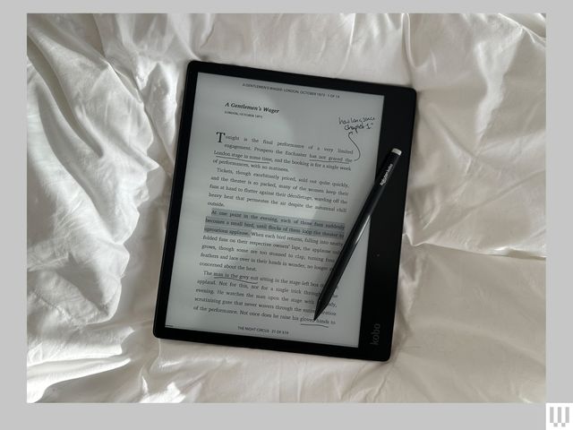 Kobo Elipsa 2E, a digital notebook with a smart pen (stylus) on top of a wrinkled white sheet with the screen showing a page from an e-book and handwritten notes scribbled in the margins
