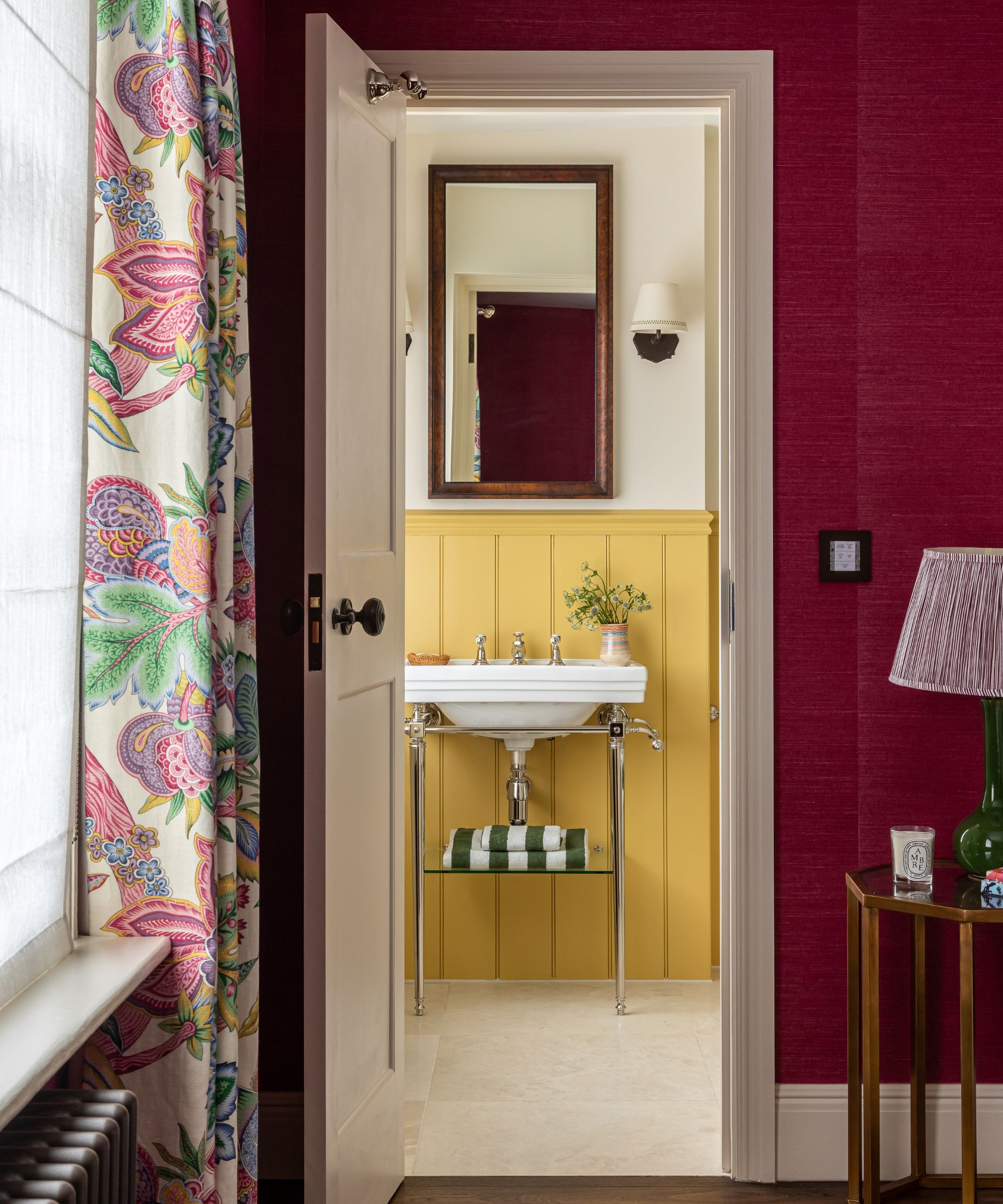 A doorway, surrounded by red wallpaper, leading to a bathroom with yellow paint