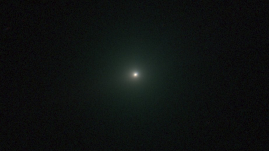 An image of comet 3I/ATLAS appearing as a white dot with a green hue.