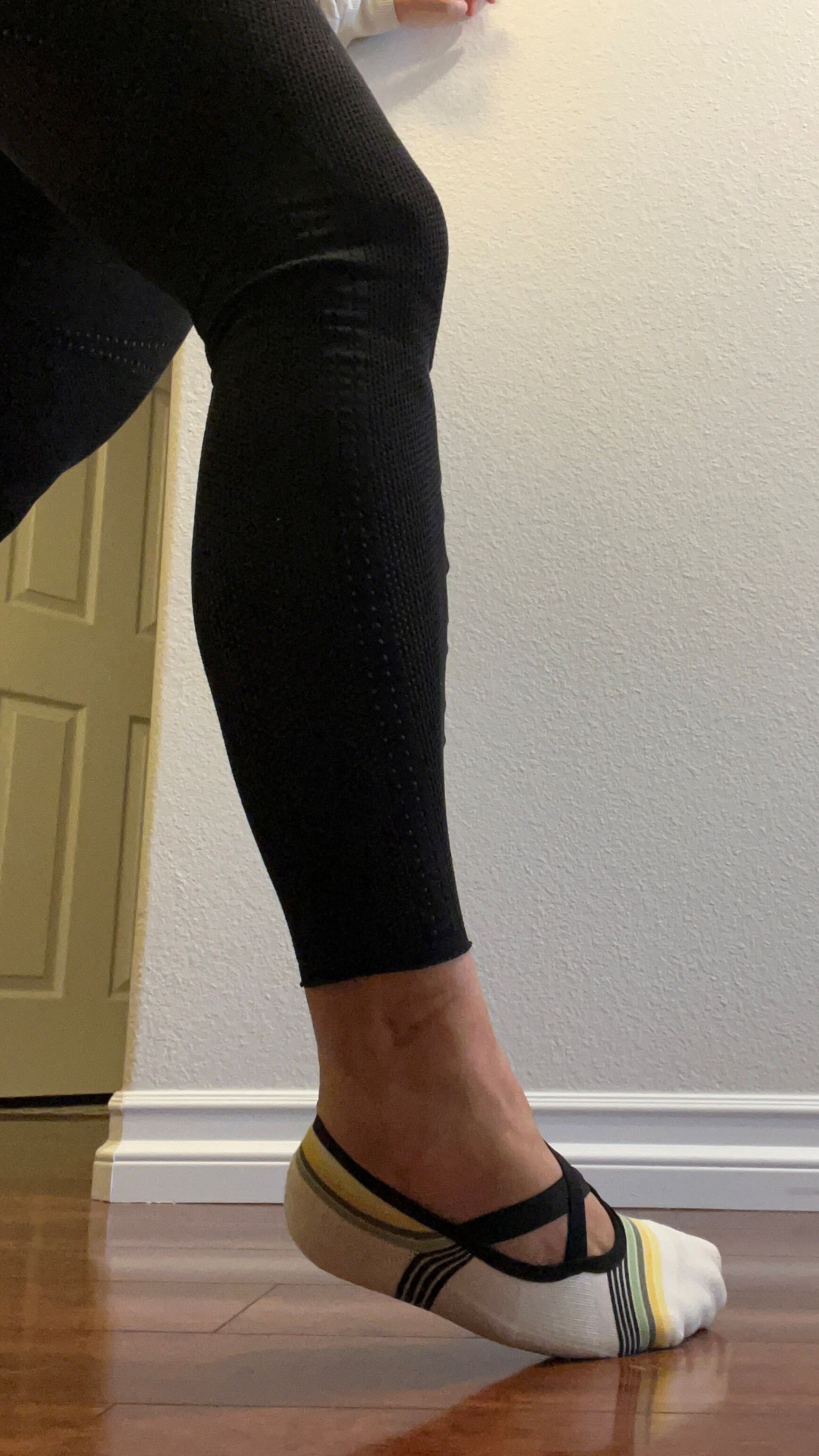 A leg in black leggings seen from the thigh down, with the heel raised and foot rolled to the outside