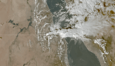 An aerial view of smoky material above two landforms separated by a river.