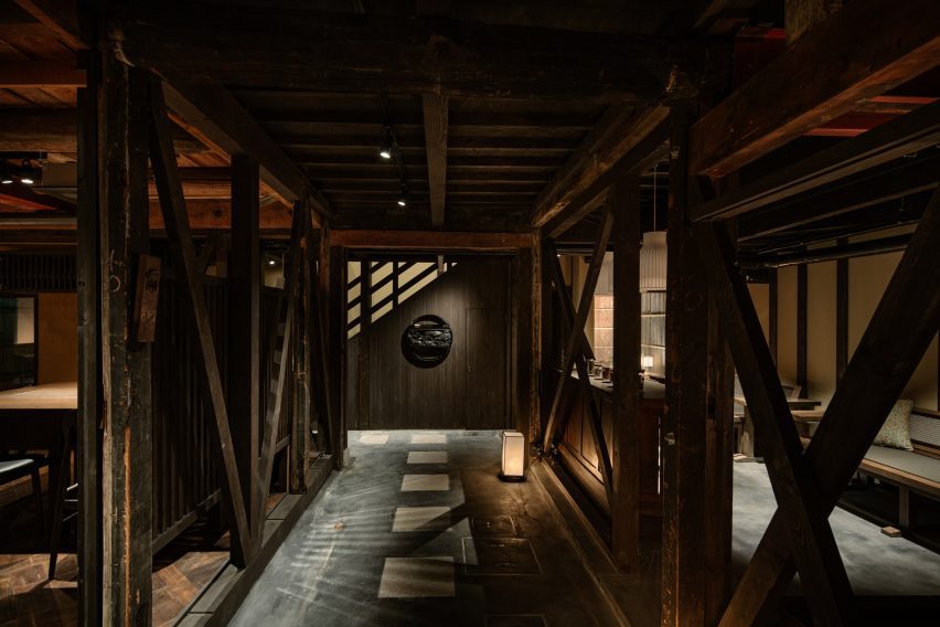 Photograph of a dark, warmly lit corridor made with timber beam structures separating two living areas of the house.