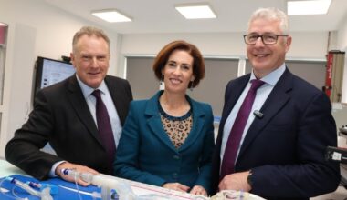 A woman and two men stand in a lab looking at equipment on a table.