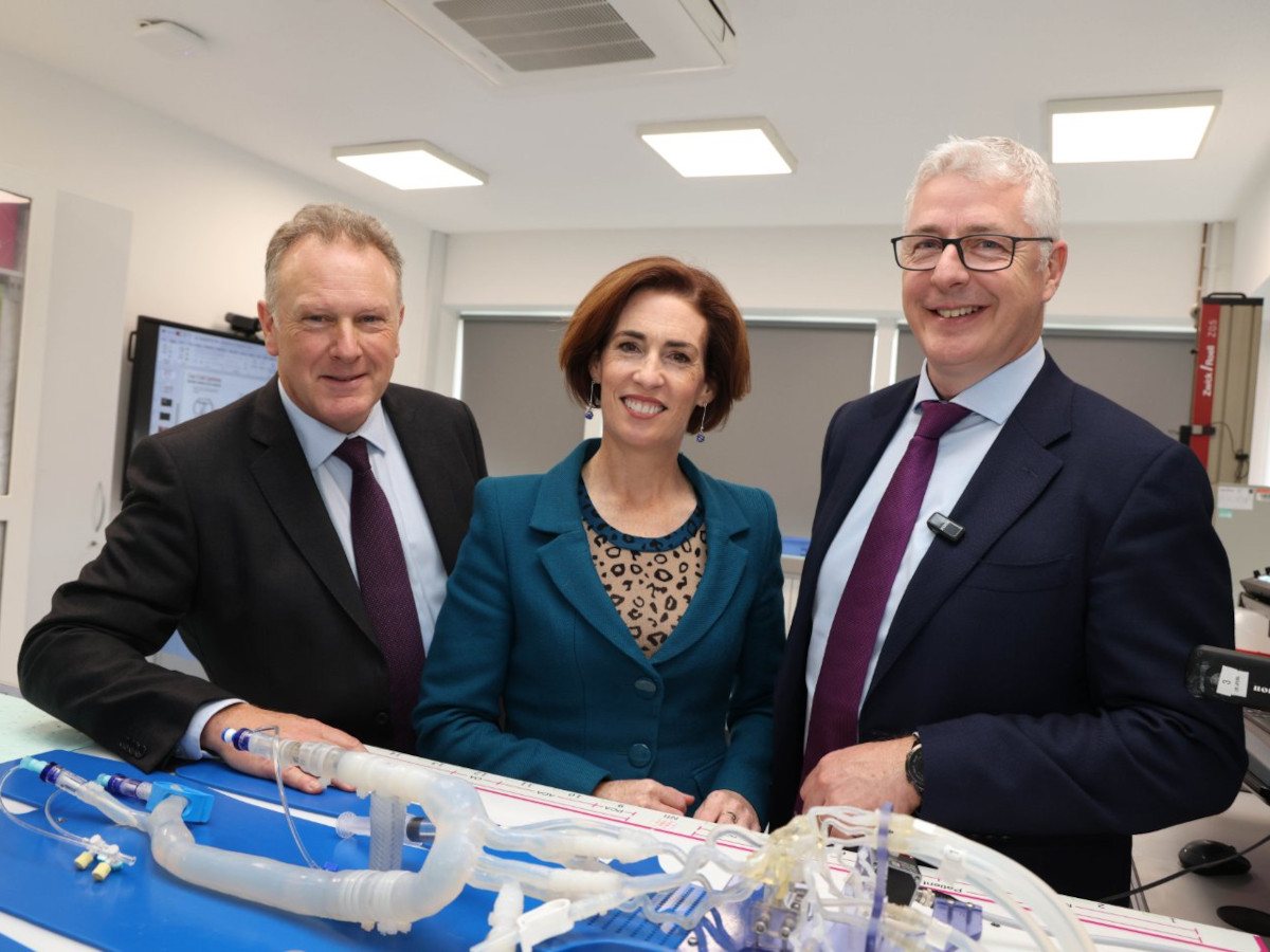 A woman and two men stand in a lab looking at equipment on a table.