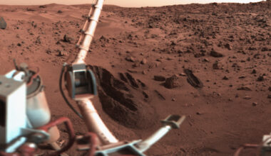 Life on Mars: Part of machine with robotic arm on left, with reddish rocks and sand dunes in background.