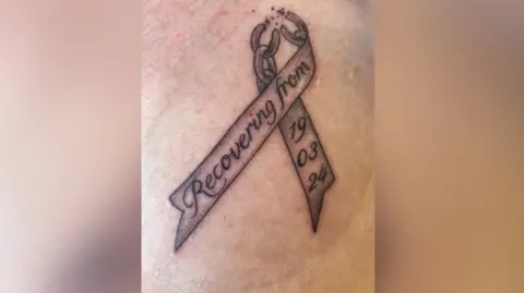 John Wade Tattoo on skin with words - recovering from 19/03/24.