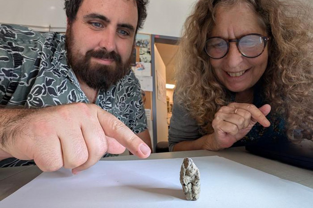 Two archaeologists pointing at an ancient figurine depicting a goose embracing a woman.