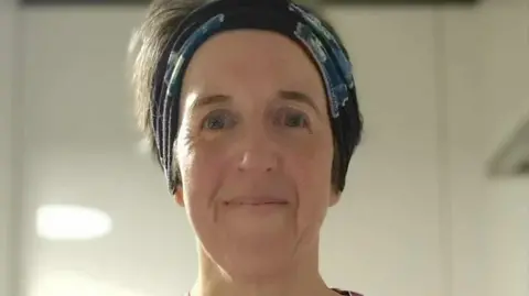 Jen Gray Jen Gray smiling at the camera. She is wearing a black headband. 