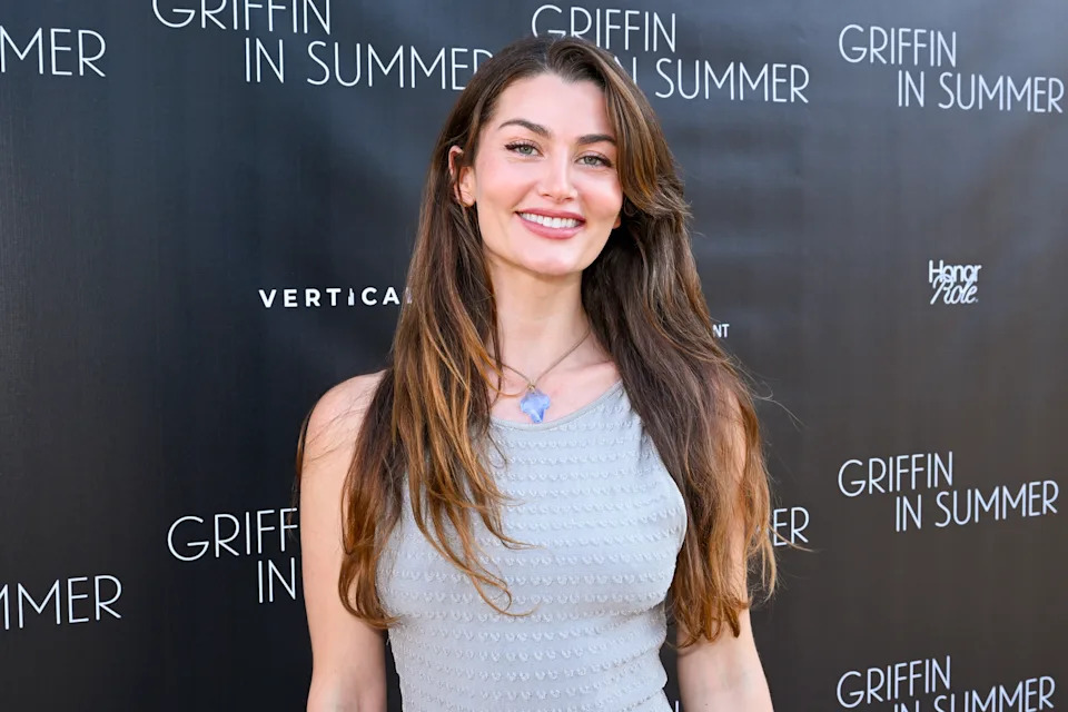 Person smiling at an event, wearing a sleeveless textured dress, against a backdrop with repeated text "Griffin in Summer."