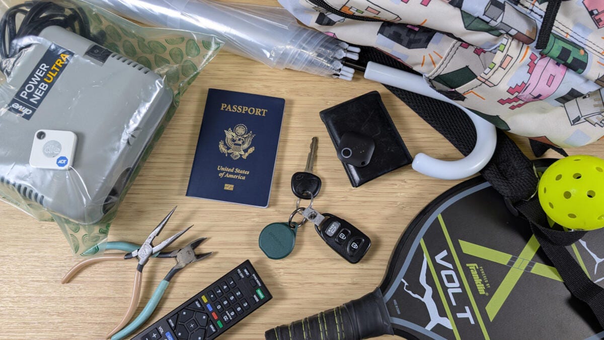 bluetooth trackers and various trackable items on bamboo desk including a passport, car keys, and umbrella