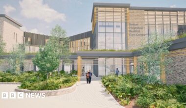 Architectural drawing of the Boston Integrated Health and Care Centre, showing a modern building with large glass windows, stone walls, and wooden accents. The entrance is framed by landscaped greenery and a paved walkway, with a few people walking toward the main doors under a covered structure.