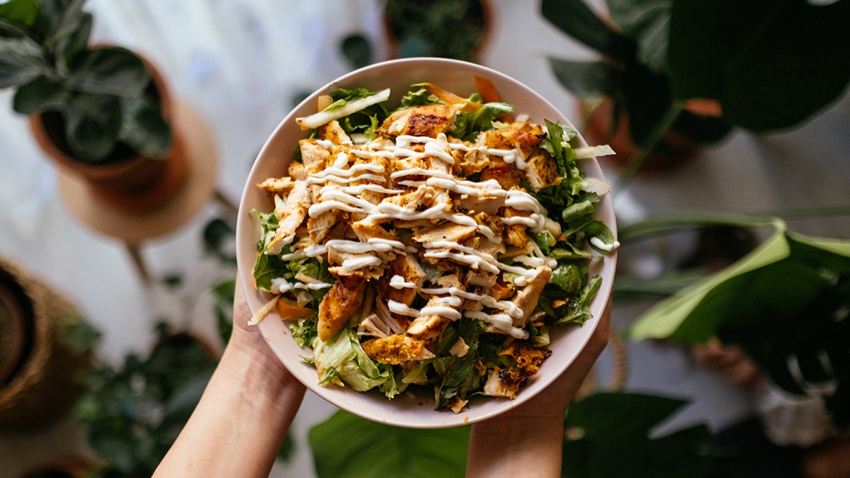 A green salad in a bowl with chicken and creamy dressing