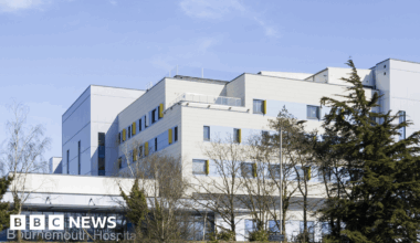 The Beach building at Royal Bournemouth Hospital, as seen from distance. The white, multi-storey, compartmented building sits on a grassy bank behind trees.